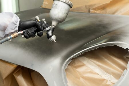 Facharbeiter trägt mit einer Spritzpistole eine industrielle Lackierung auf eine Metalloberfläche auf, präzise und gleichmäßig.