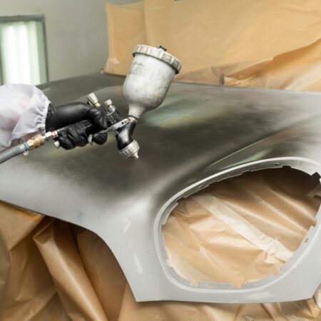 Facharbeiter trägt mit einer Spritzpistole eine industrielle Lackierung auf eine Metalloberfläche auf, präzise und gleichmäßig.